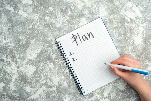 Overhead view of hand writing on spiral notebook on gray background