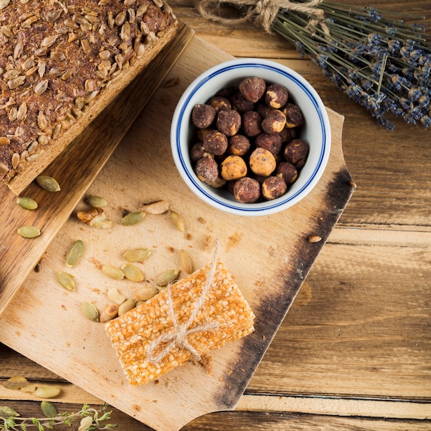 Free Photo an overhead view of hazelnut bowl with bread and sesame bar on chopping board