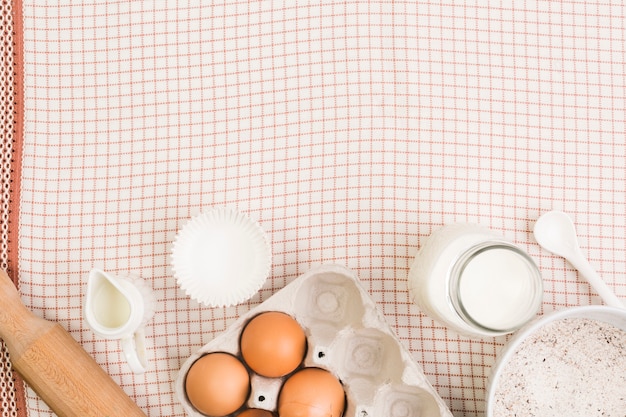 Free photo overhead view of healthy ingredients with rolling pin; muffin mold and spoon on white and red surface