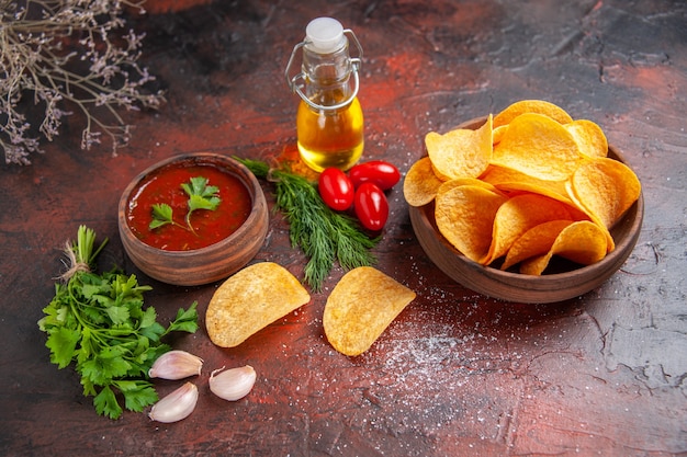 Free Photo overhead view of homemade delicious potato crispy chips in a small brown bowl oil bottle green tomatoes garlic ketchup and chopped pepper on dark table