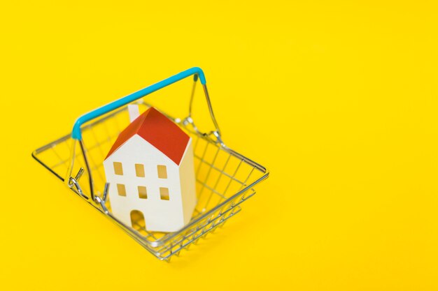 An overhead view of house model inside the shopping cart against yellow background