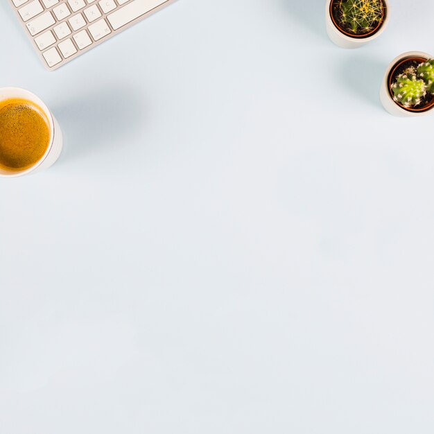 An overhead view of keyboard; cup of coffee and cactus plant on white background