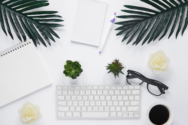 Free photo an overhead view of keyboard with office stationery and leaves on white background