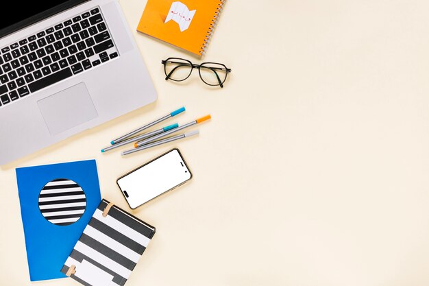 Overhead view of laptop and cellphone with stationery on colored background