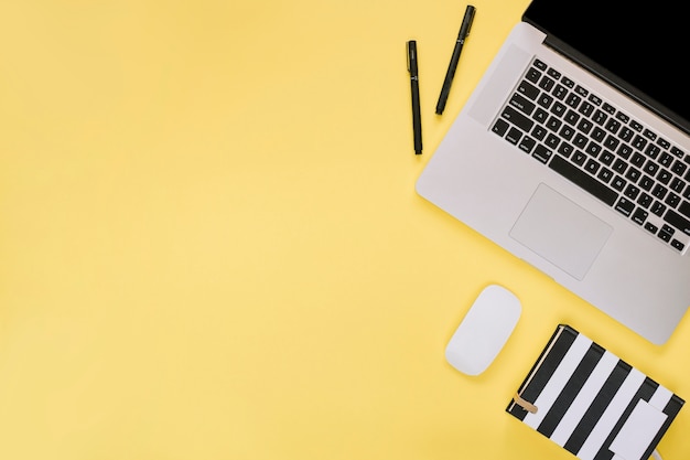 Overhead view of laptop and stationeries on yellow surface