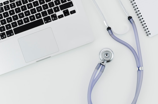 Free photo an overhead view of laptop with stethoscope and spiral notebook on white desk