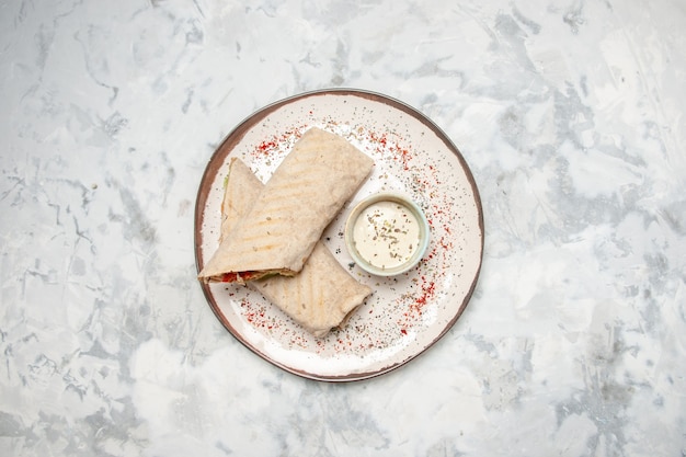 Overhead view of lavash wrap and yogurt in a small bowl on a plate on stained white surface with free space