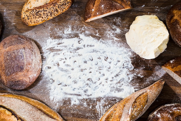 Free photo an overhead view of loaf of bread; baguette and kneaded dough with flour on wooden desk