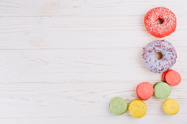 Free photo an overhead view of macaroons and donuts on wooden texture background