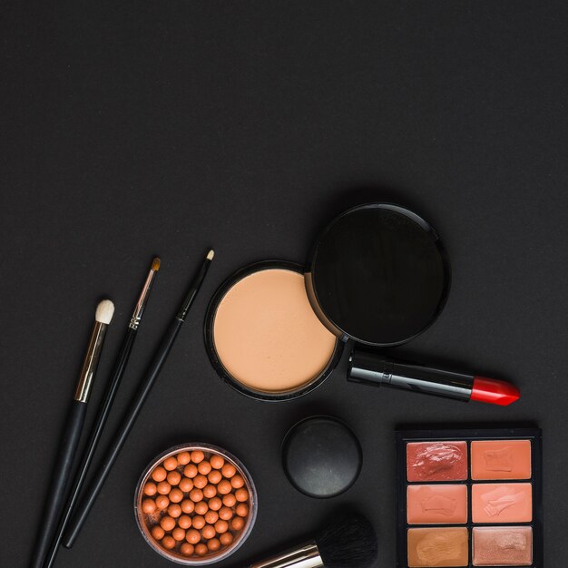 Overhead view of makeup products with brushes on black backdrop