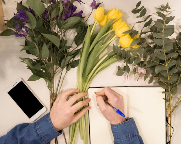 Free Photo an overhead view of a male florist writing on diary with pen on table with flowers