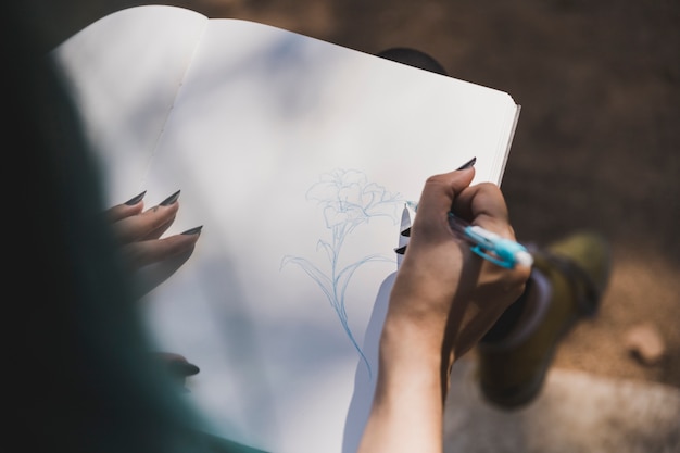 An overhead view of man's hand drawing flower on notebook