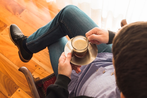 An overhead view of a man sitting on arm chair holding cup of coffee