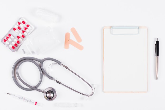 Overhead view of medical equipments with paper on clipboard and pen on white backdrop