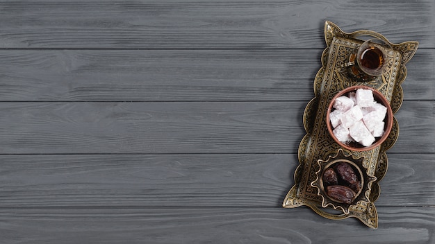 An overhead view of metallic tray with turkish delight lukum; dates and tea on ramadan over the wooden table