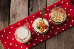 Free photo overhead view of milk, yogurt and dry oats in the glass jar on red napkin over the wooden table