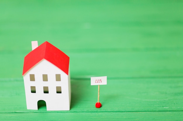 An overhead view of miniature house model near the sale tag on green textured background