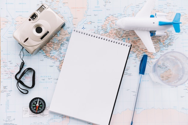 Free Photo an overhead view of miniature white airplane; spiral blank notepad; pen; camera and compass on map