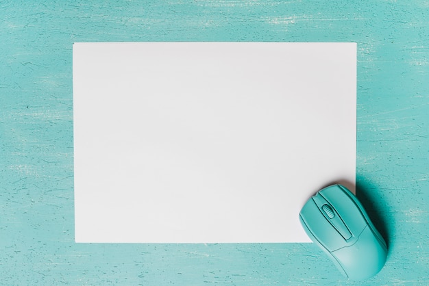 An overhead view of mouse on blank white paper against turquoise background