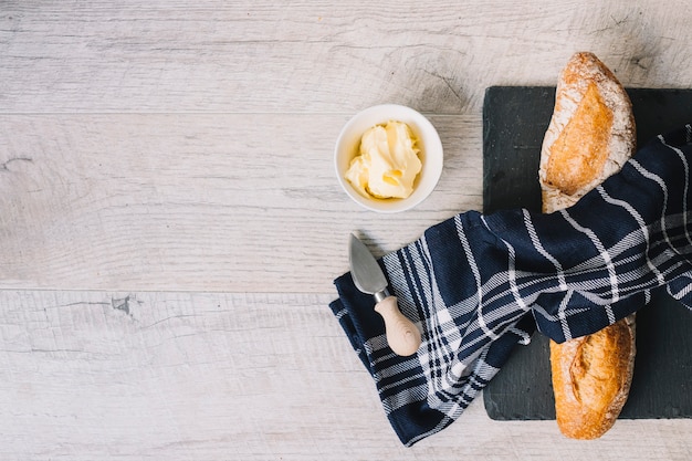 Free photo an overhead view of napkin over the baked baguette; butter; knife on white wooden backdrop