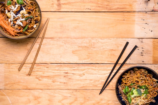 Free photo an overhead view of noodles bowls with chopsticks on wooden plank