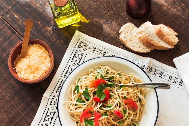 An overhead view of noodles with cheese and bread slice on wooden background