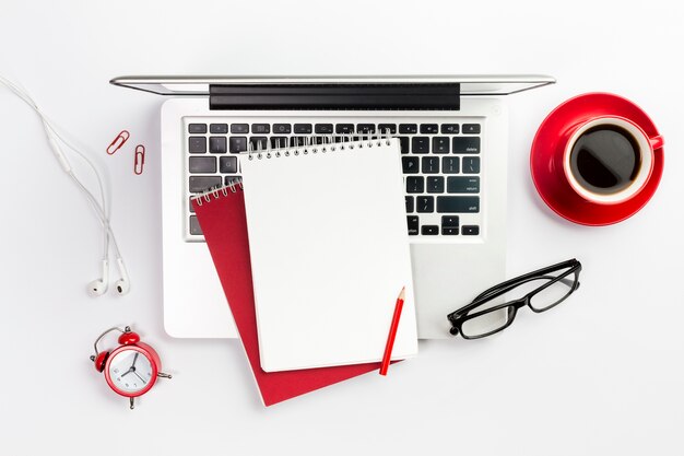 Overhead view of office supplies,laptop,coffee cup,alarm clock and spectacles over white desk