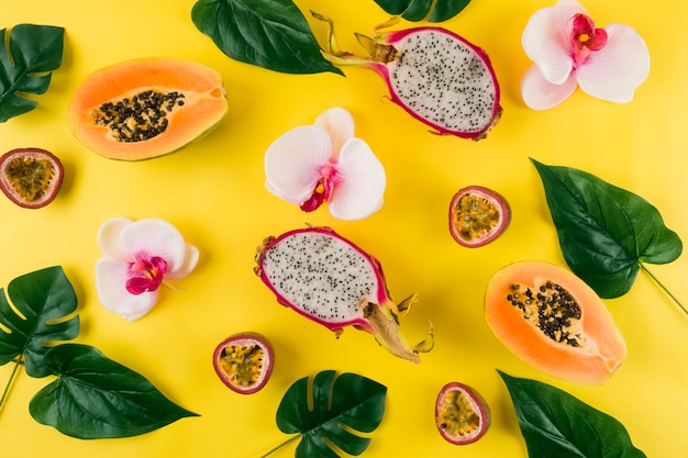 Free Photo an overhead view of orchid flower; leaves; dragon fruit and papaya on yellow backdrop