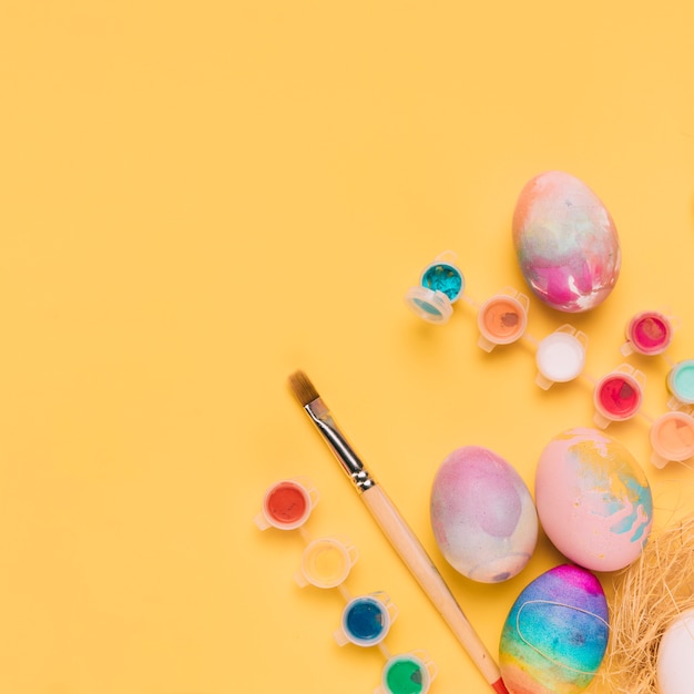 An overhead view of painted easter eggs; paint brush and water color paint on yellow backdrop