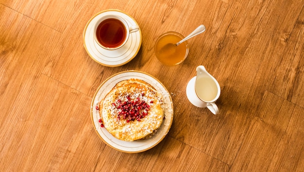 Overhead view of pancake with honey and tea cup on wooden table