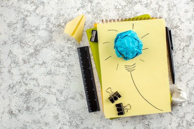 Free Photo overhead view of paper light bulb on closed spiral notebooks and office appliances on the left side on white surface