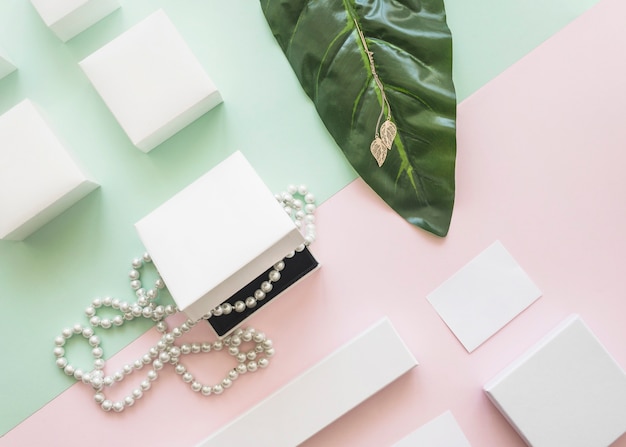 Free photo overhead view of pearl necklace and golden earrings with white boxes on paper background