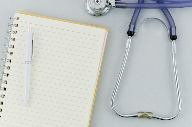 Free photo an overhead view of pen over spiral notebook and stethoscope on grey background