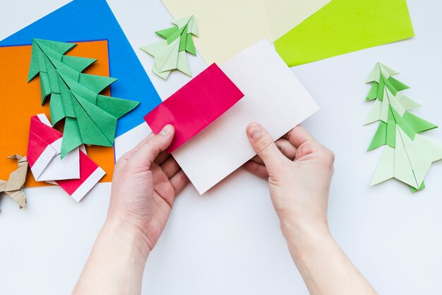 An overhead view of a person's hand making the craft with paper on white backdrop