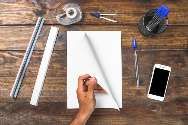 Overhead view of a person turning page with stationery and mobile phone on table