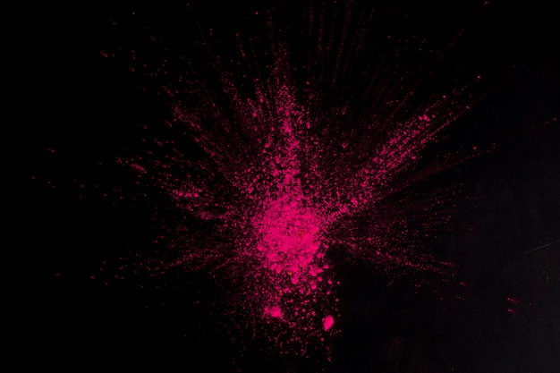 Overhead view of pink color exploding on black surface