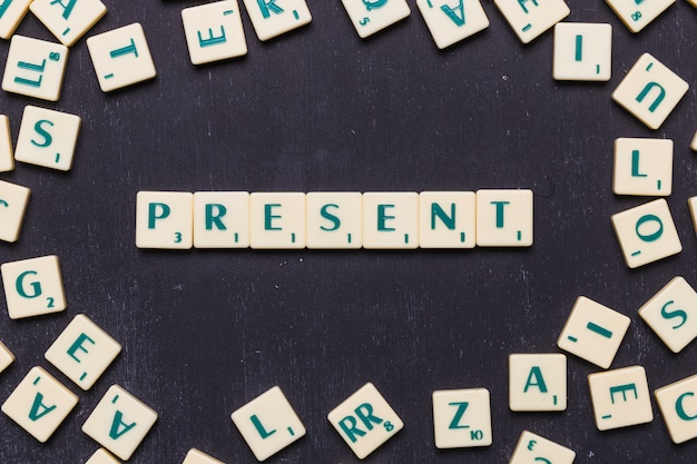 Overhead view of present text on scrabble letters over black backdrop