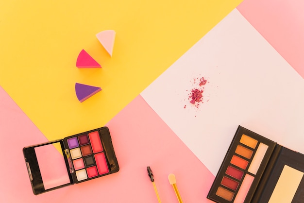 Free photo an overhead view of professional make-up tools and eyeshadow palette on colorful background