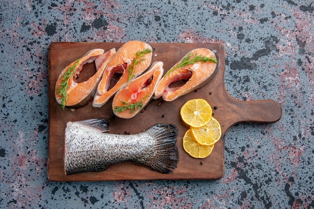 Free photo overhead view of raw fishes lemon slices greens pepper on wooden cutting board on blue black mix colors table