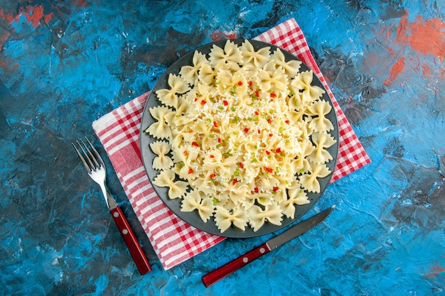 Free Photo overhead view of raw italian farfalle pasta on red stripped towel and cutlery set on blue table