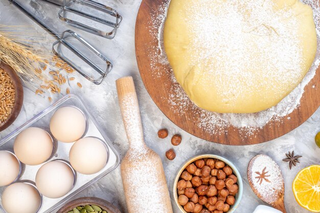 Overhead view of raw pastry flour on round board hazelnuts eggs lemon on stained white background