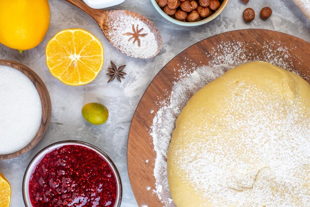 Overhead view of raw pastry flour on round board wooden spoon oatmeal fresh fruits jam sugar on stained white background