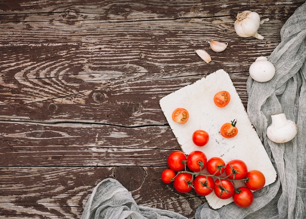 An overhead view of red cherry tomatoes; garlic cloves and mushroom on wooden table