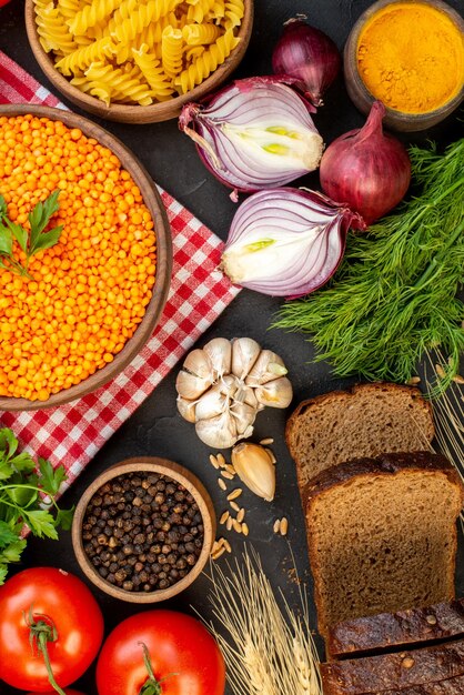 Overhead view of red lentils in a brown bowl on towel tomato with stem fallen oil bottle salt green bundle dried pepper