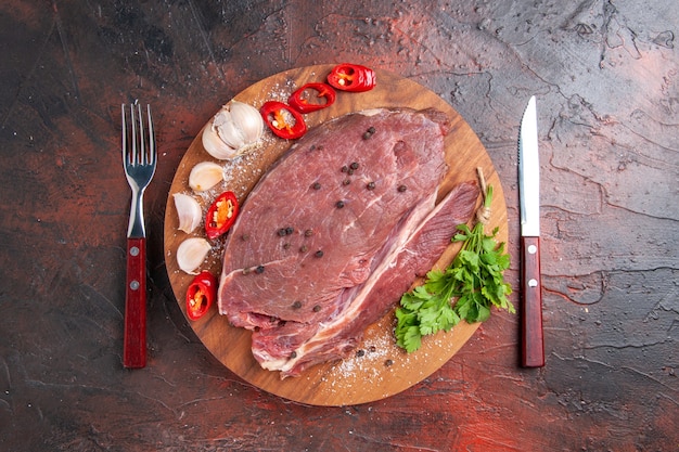 Overhead view of red meat on wooden tray and garlic green lemon pepper onion fork and knife on dark background