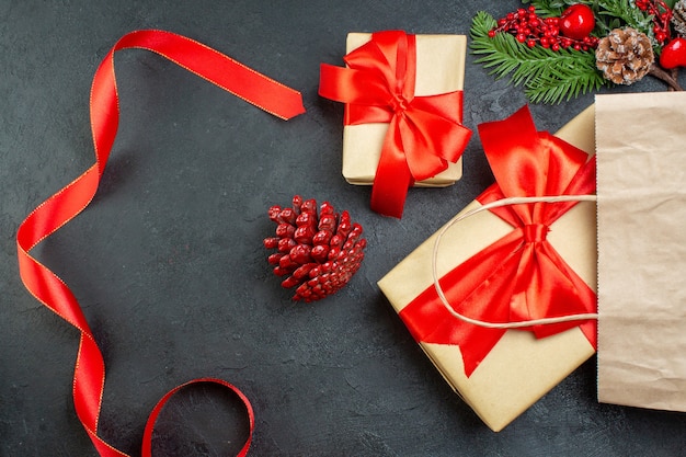 Overhead view of a roll of red ribbon conifer cones and gift fir branches on dark table