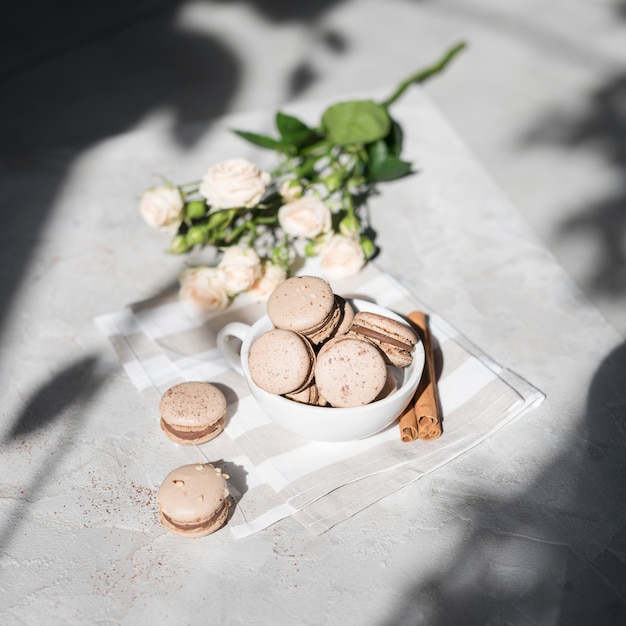 An overhead view of rose bouquet with cinnamon macaroons in white cup on grey concrete textured backdrop