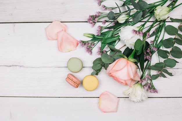 Free Photo an overhead view of rose; limonium and eustoma flowers bouquet with macaroons on white wooden desk