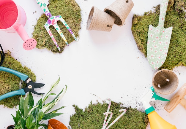 Free photo overhead view shovel; gardening fork; pruner; watering can; turf; spray bottle on white backdrop