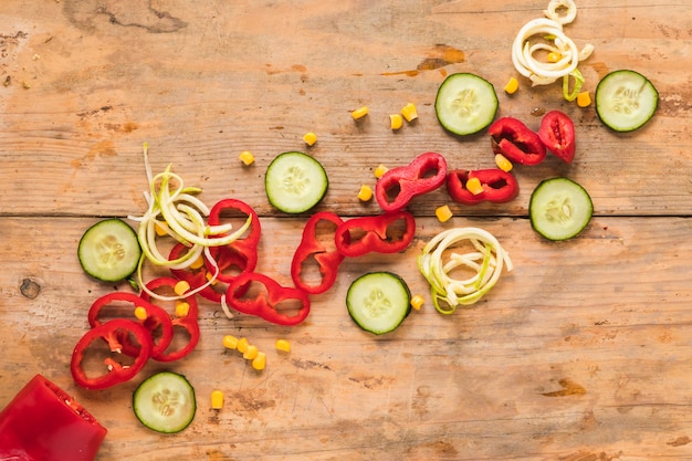 Free photo an overhead view of slice paprika; cucumber and corn on wooden table